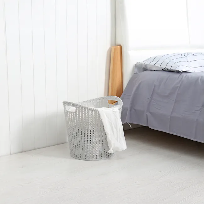 Alice Laundry Basket - Grey - 3 - White wooden wall, light wooden floor, white laundry basket, white clothes, gray bed