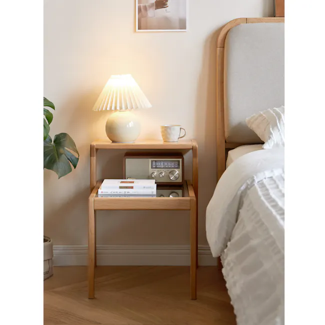 Lorren Two Tier Bedside Table - 4 - Wooden nightstand with lamp, white mug, radio, books, green plant, beige wall, wooden