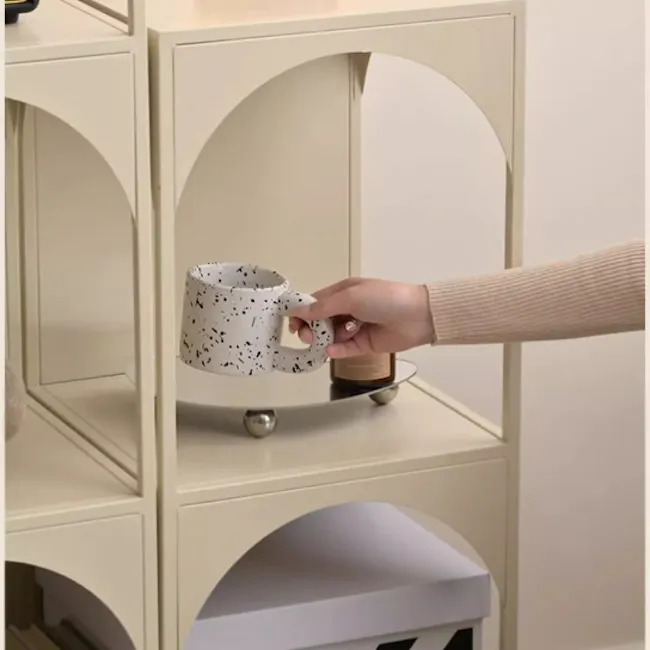 Novi Arch 3-Tier Storage Shelf - Cream - 6 - Hand holding a white mug with black speckles., Interior setting with a beige