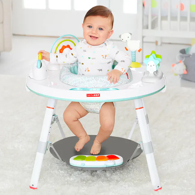 Skip Hop Activity Center - Silver Lining Cloud 3 Stage - 5 - Baby sitting in a colorful baby bouncer, wearing a white onesie