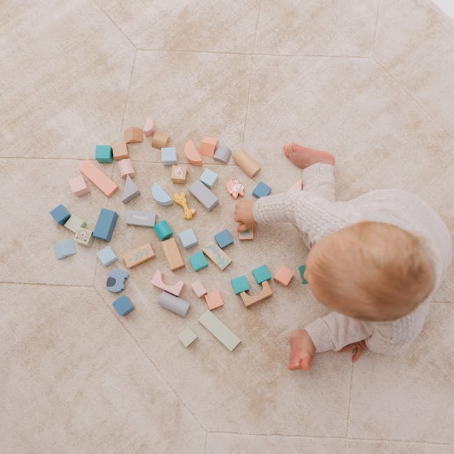 Bubble Wooden Activity Blocks - 10 - Soft, pastel-colored wooden blocks scattered on a beige carpet, baby's hand picking up