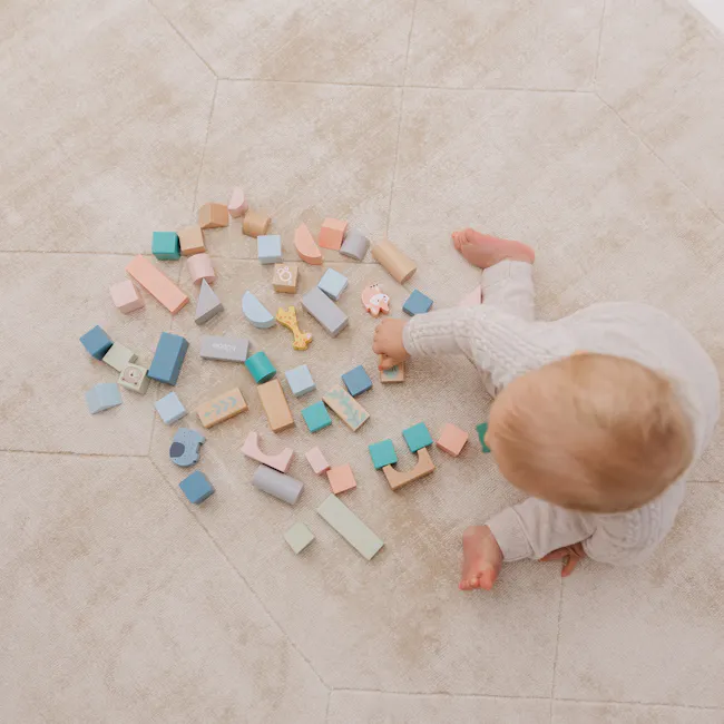 Bubble Wooden Activity Blocks - 10 - Soft, pastel-colored wooden blocks scattered on a beige carpet, baby's hand picking up