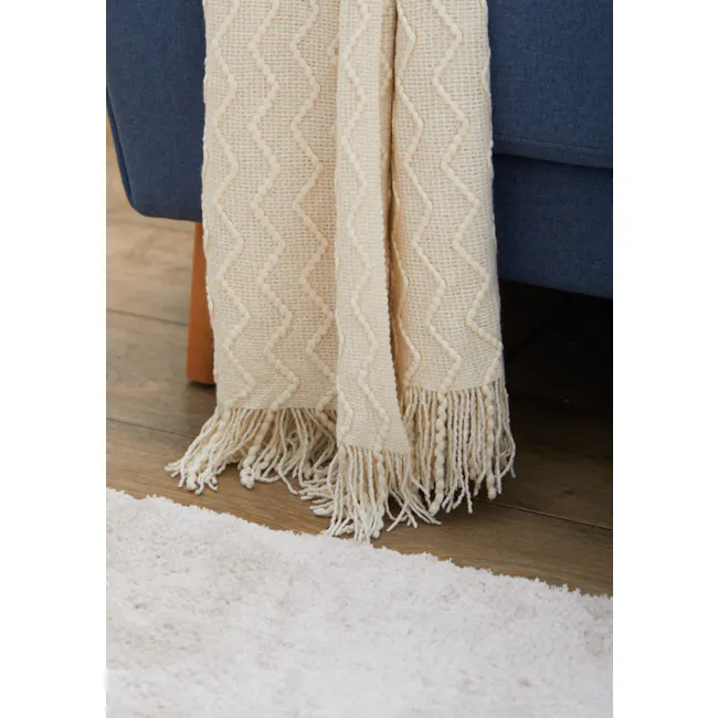 Havre Throw - Off White - 3 - Cream-colored knitted throw blanket with zigzag pattern and fringed edges, draped over a