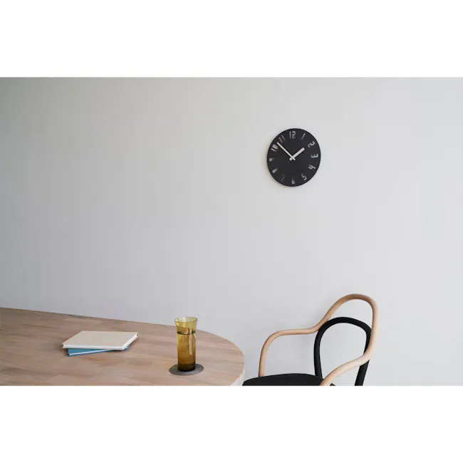 PANECO CLOCK - SAND Dark Gray - 4 - Wooden desk, black clock, minimalist design, white wall, light wooden table, stack of