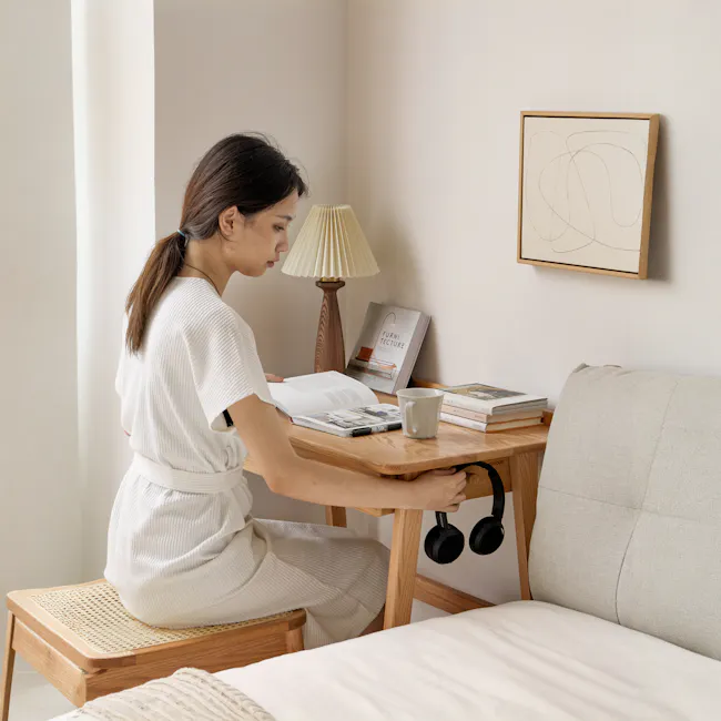 Chase Study Table 1m - 5 - White knit dress, wooden table, beige wall, open book, black headphones, beige sofa