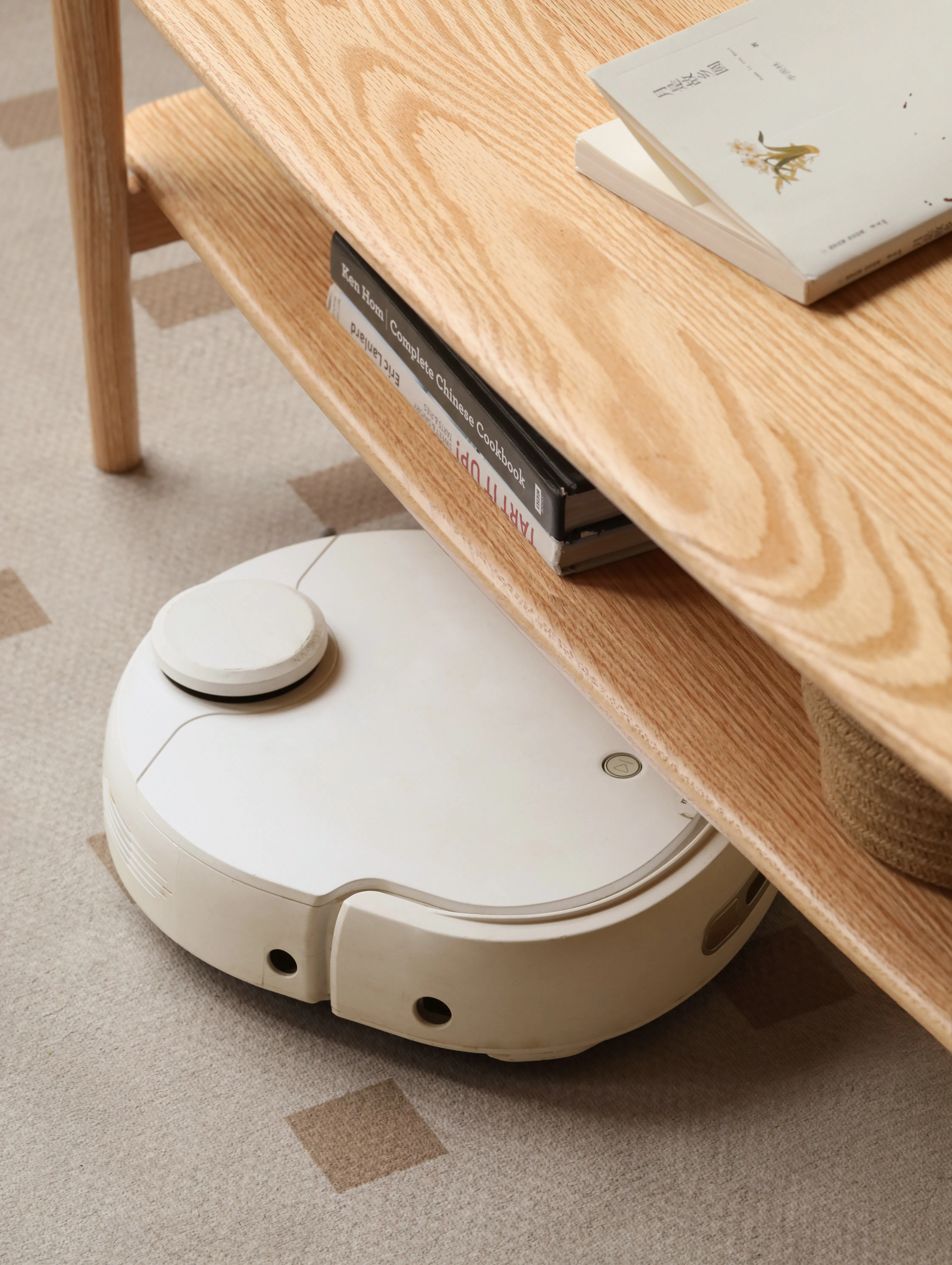 Nigel Narrow Coffee Table 1m - 13 - Wooden coffee table, stack of books, white robotic vacuum cleaner, beige carpet, modern
