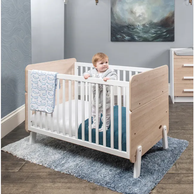 Natty Boori Cot Bed - Barley & Oak - 2 - White crib with blue accents, wooden frame, blue blanket, light gray walls, wooden
