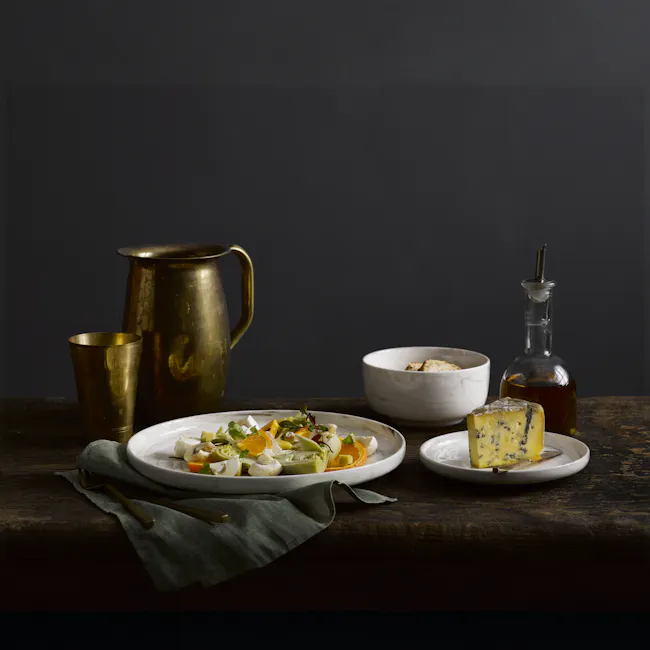 Luzerne Marble Deep Round Coupe Plate (2 Sizes) - 3 - Golden metal pitcher, white marble plate, fresh salad, orange slices