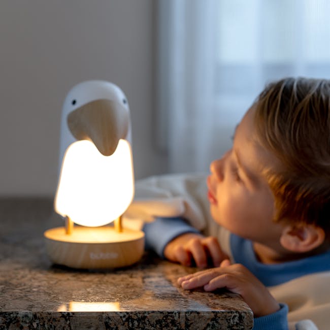 Bubble Toucan Night Light - 8 - Lamp with bird-shaped base, child looking at glowing lamp, cozy indoor setting, soft