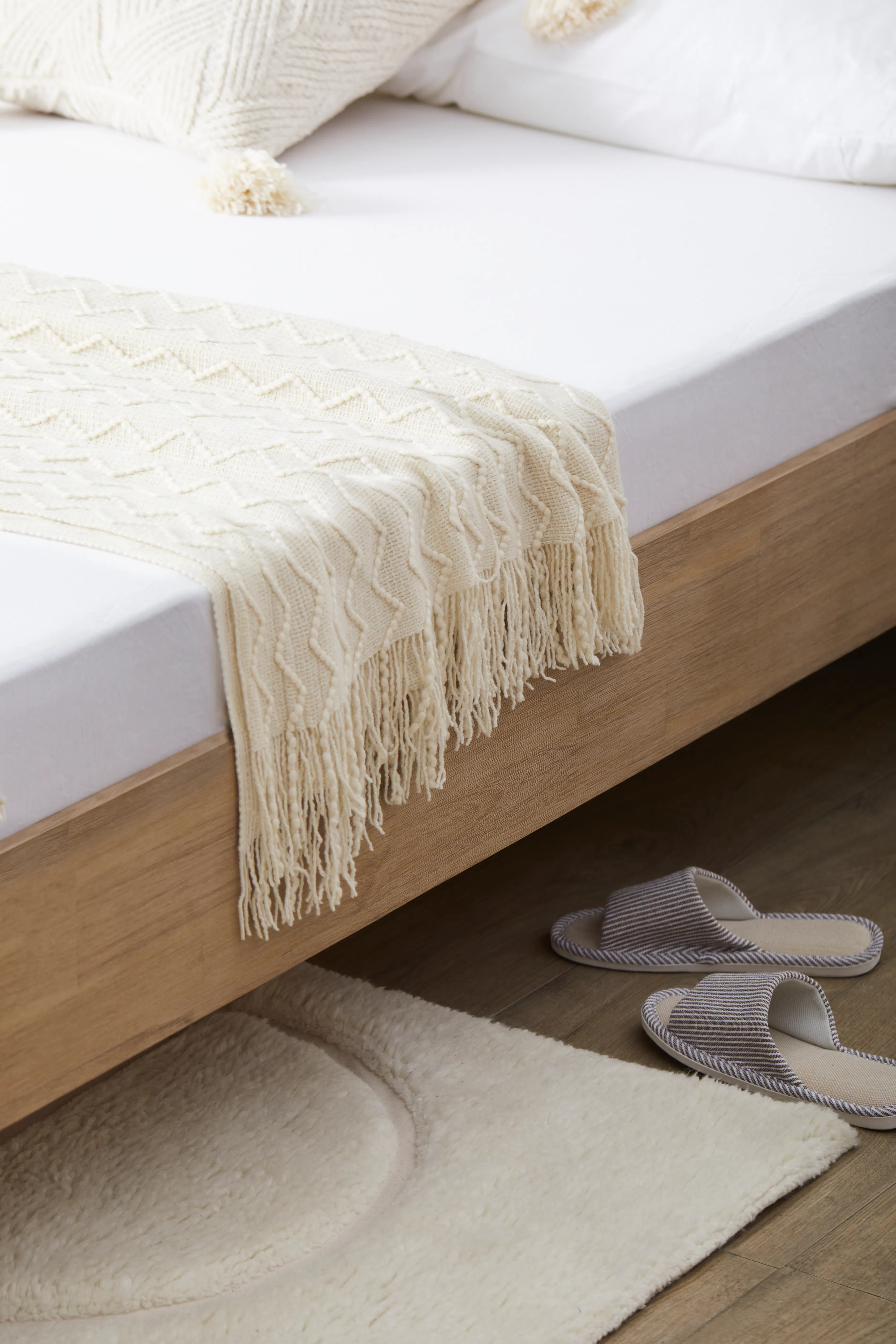Catania Queen Bed - 15 - Cream-colored knitted blanket with fringe, wooden bed frame, white bedding, fluffy white rug
