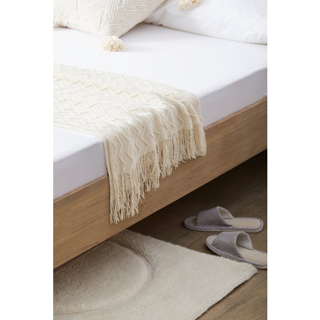 Catania Queen Bed - 11 - Cream-colored knitted blanket with fringe, wooden bed frame, white bedding, fluffy white rug