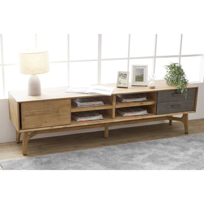 Hudson TV Console 2m - 3 - Lamp with textured beige shade, wooden side table, open book, white candle holder, green potted
