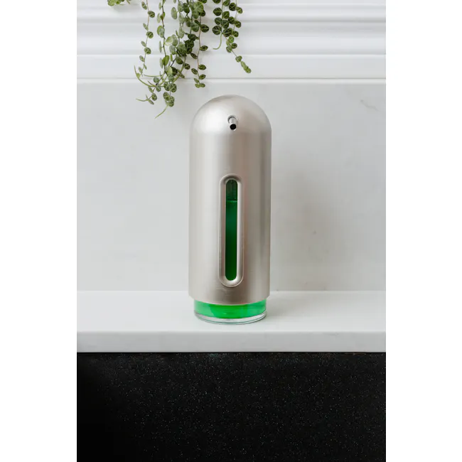 Penguin Soap Pump - Nickel - 3 - Silver cylindrical device, green liquid inside, white marble countertop, modern design