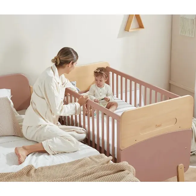 Neat Boori 5 in 1 Cot Bed - Cherry - 3 - Woman in white pajamas sitting on bed, interacting with baby in crib, wooden crib