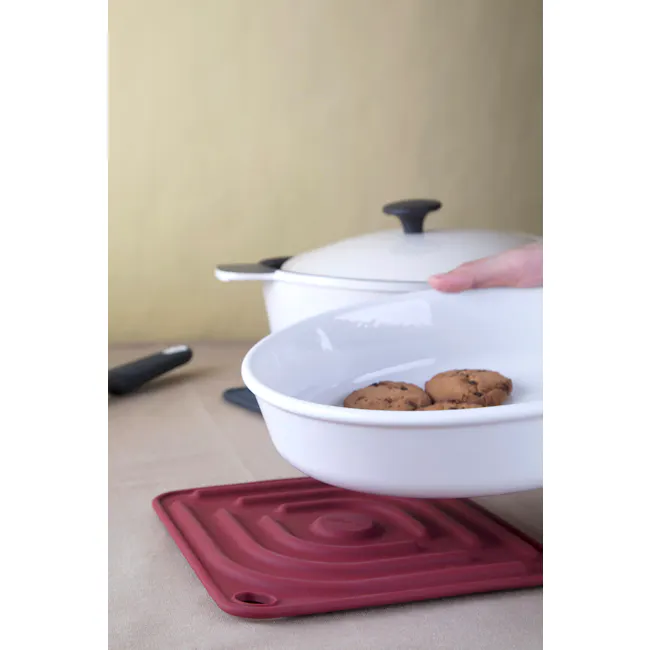 Cookduo Air Trivet - Red - 2 - White bowl with chocolate chip cookies, hand placing cookies, maroon silicone mat, white pot