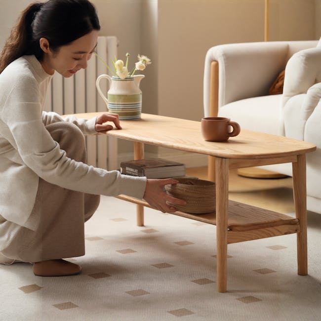 Nigel Narrow Coffee Table 1m - 8 - Light brown wooden coffee table, beige carpet with brown diamond patterns, person wearing