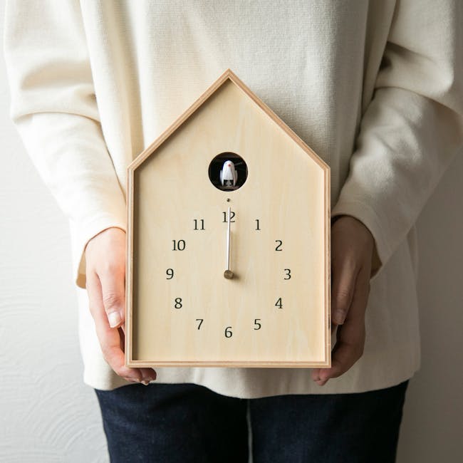 Birdhouse Clock - Natural - 2 - Wooden clock with a small figurine inside, held by a person wearing a cream-colored sweater