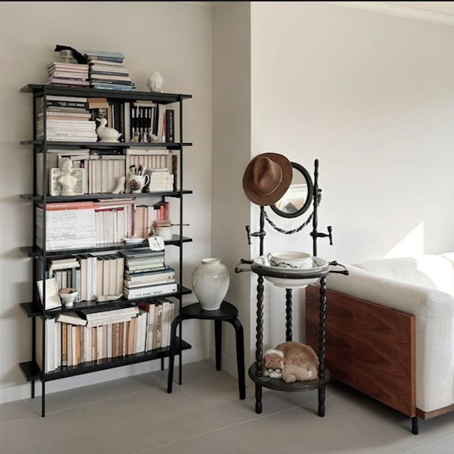 Fraser Bookshelf - 6 - Black metal bookshelf filled with books, decorative items, and a white bird statue. Wooden stool
