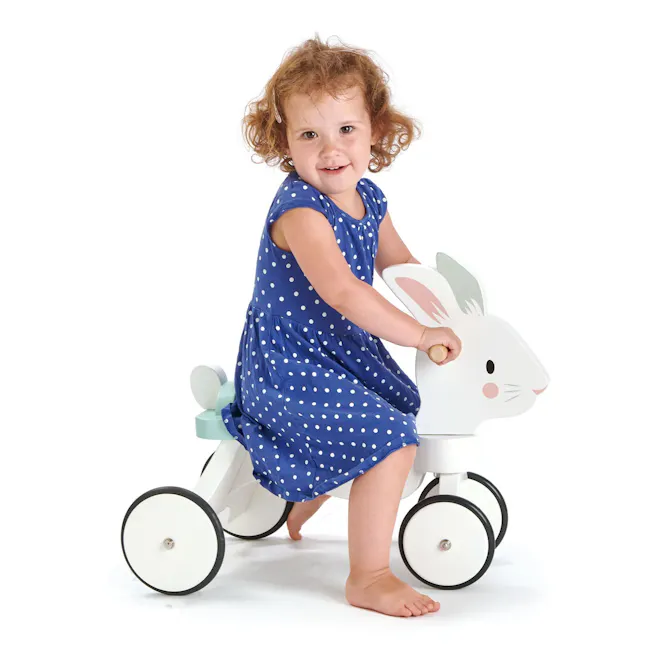 Tender Leaf Running Rabbit Ride On - 4 - Cute child in blue polka dot dress, riding a bunny-shaped pedal tricycle, barefoot
