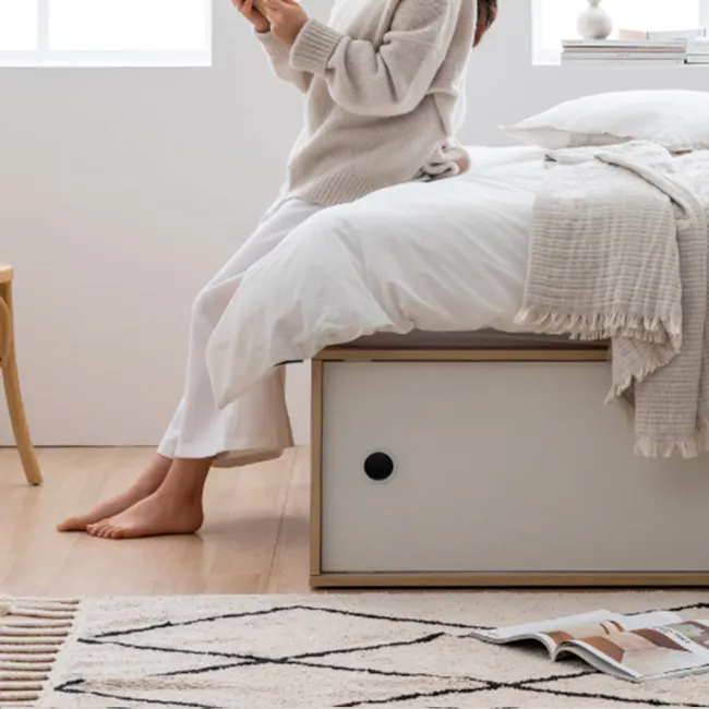 Reyna Super Single Platform Storage Bed - 5 - Sleek white bed with cozy blankets, person sitting on bed, light beige