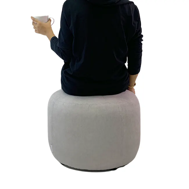 March Ottoman - Black - 6 - black hoodie, gray ottoman, person sitting, white mug, indoor setting, casual attire, back view
