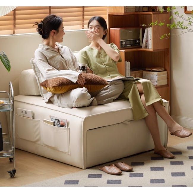 Tilly Lounge Sofa Bed - 15 - Sitting on a cream-colored sofa, two women chatting, one holding a mug, the other reading a