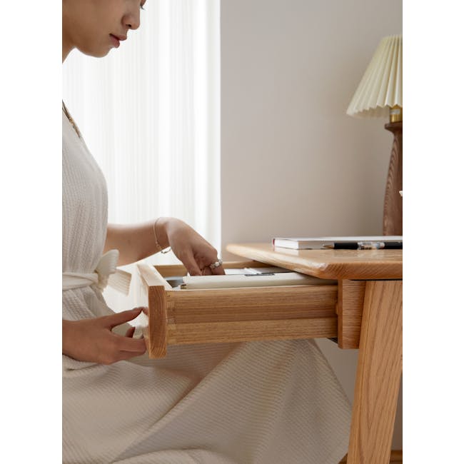 Chase Study Table 1m - 12 - White robe, wooden desk, person sitting, hands opening drawer, jewelry, pen, notebook