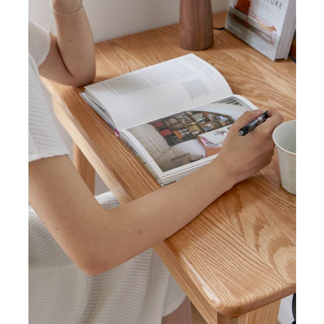 Chase Study Table 1m - 13 - Wooden table, open book, person writing, pen, white dress, wooden chair, light brown wood