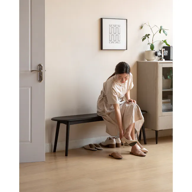 Felda Bench 1.4m - Black Ash - 7 - Light beige dress, minimalist setting, woman sitting, adjusting shoes, natural light