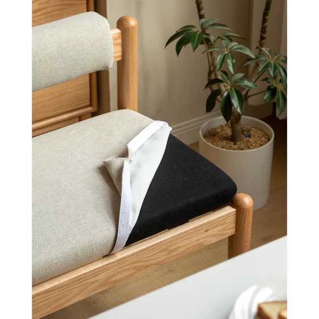 Niel Bench 1.25m - Oak, Gravel White - 5 - Wooden chair with beige and black fabric, white fabric napkin, natural light