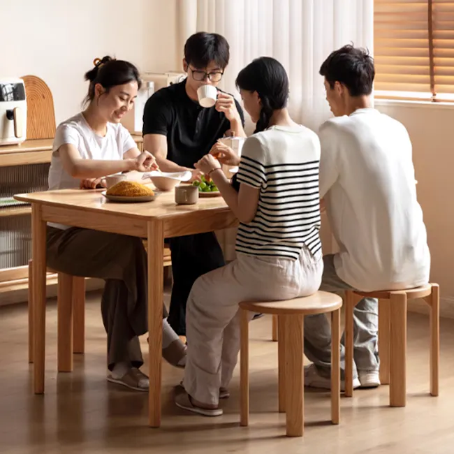 Coree Stackable Stool Set / Side Table - Oak - 4 - Group of four people sitting around a wooden dining table, enjoying a