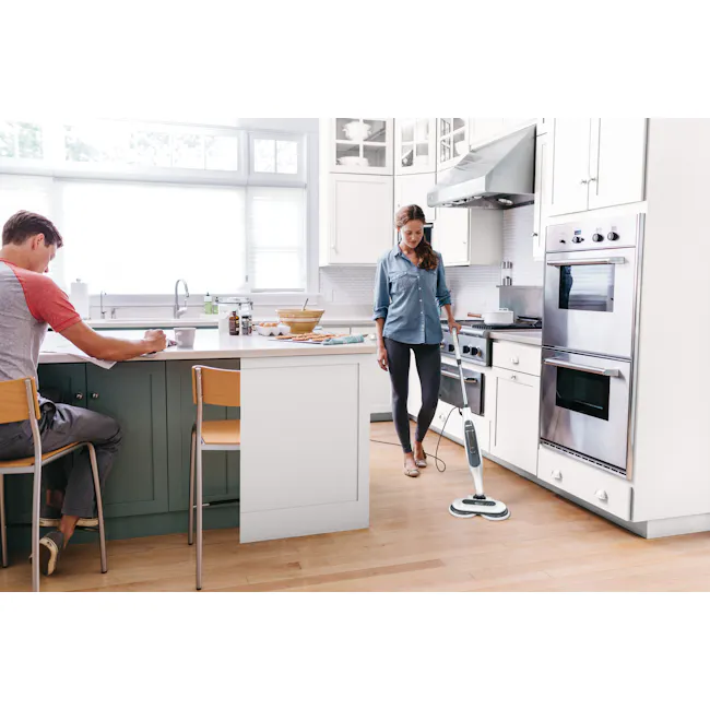 Shark Steam and Scrub Mop - 3 - Kitchen scene with two individuals, man and woman, engaged in different activities. Woman is