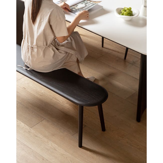 Felda Bench 1.6m - Black Ash - 8 - Light beige dress, woman sitting, reading magazine, green grapes on table, wooden floor
