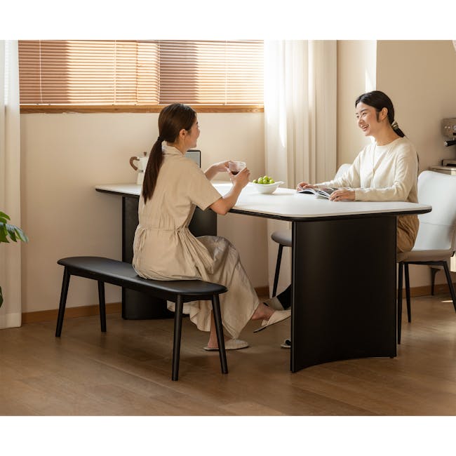Felda Bench 1.6m - Black Ash - 2 - Sunlit room, two women, sitting at table, one holding cup, other reading book, modern