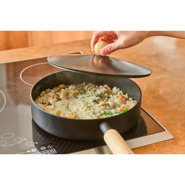 Goodle 24cm Frying Pan Lid - 2 - Hand cracking an egg over a pan filled with a creamy rice dish, wooden-handled pan resting