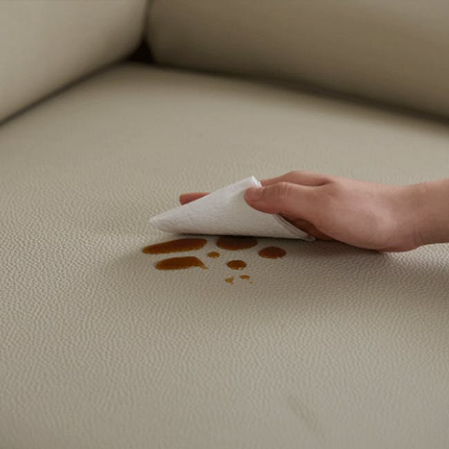 Montreal 4 Seater Sofa with Ottoman - Beige (Faux Leather) - 7 - Hand holding paper towel, brown stain on beige couch, brown