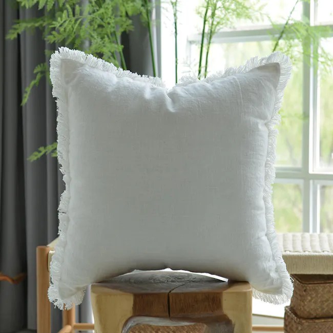 Scylla Fringe Cushion - White - 2 - White textured pillow with fringed edges, wooden stool, natural light streaming through