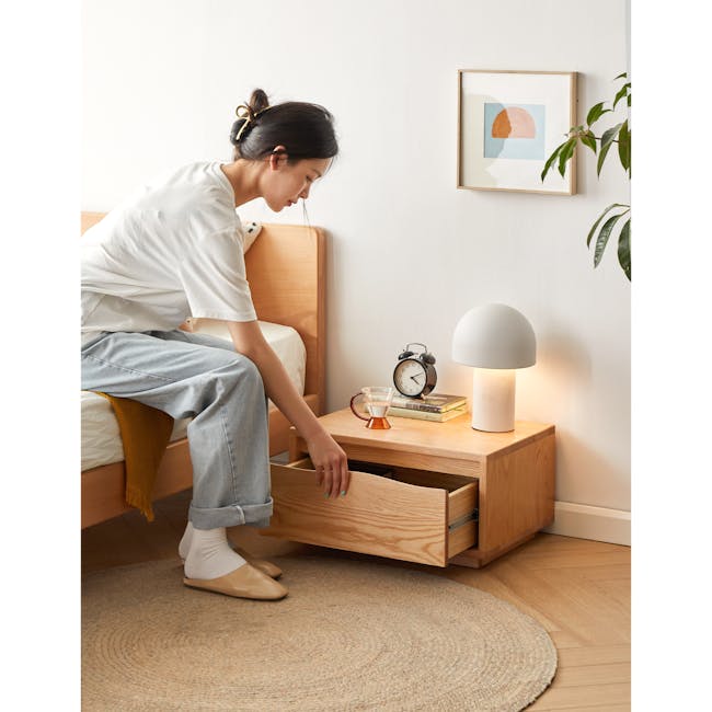 Elias Low Bedside Table - 2 - White wall, wooden bed frame, light blue jeans, white t-shirt, beige shoes, orange blanket