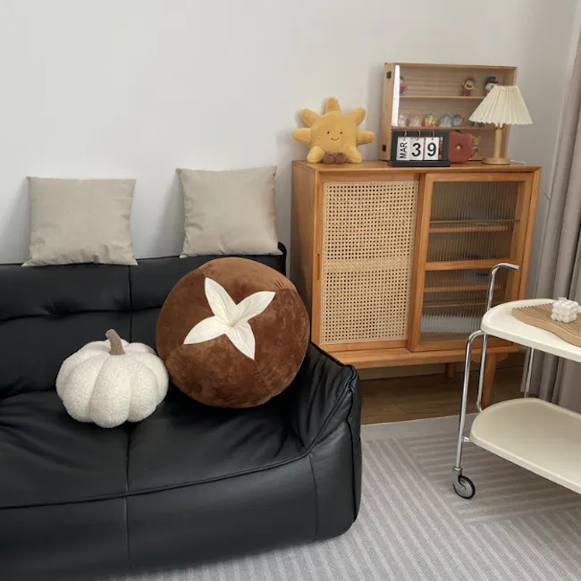 Mushroom Plush Cushion - 5 - Black leather sofa, beige pillows, brown plush pillow with white flower, white pumpkin, wooden