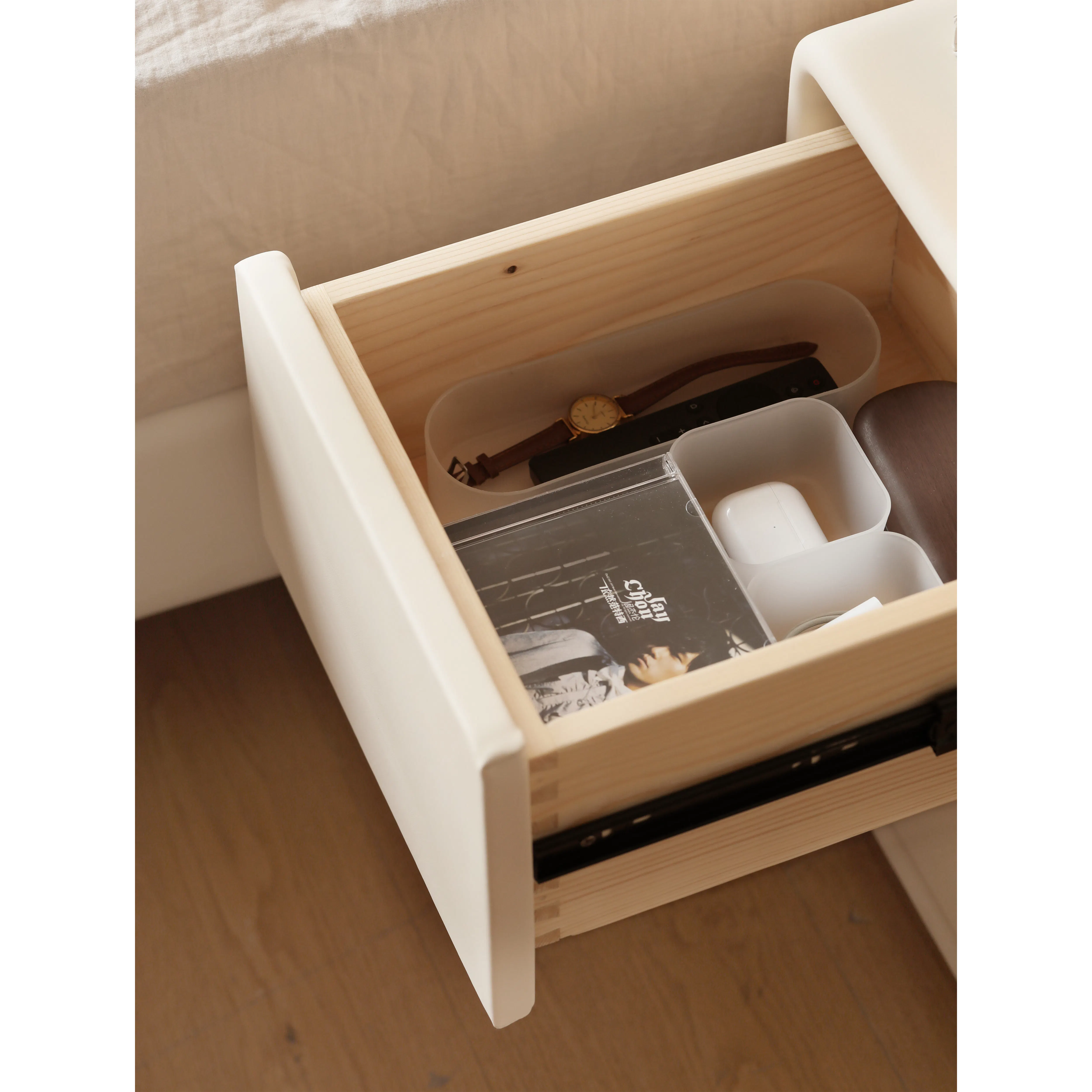 Asher Narrow Bedside Table - 9 - Wooden drawer, beige bed, white drawer pull, black and white album, brown watch, white