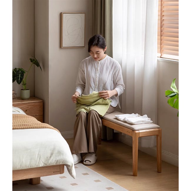 Frank Bench 1.4m - Grey (Faux Leather) - 6 - Sitting on bench, holding green garment, indoor setting, woman in white blouse