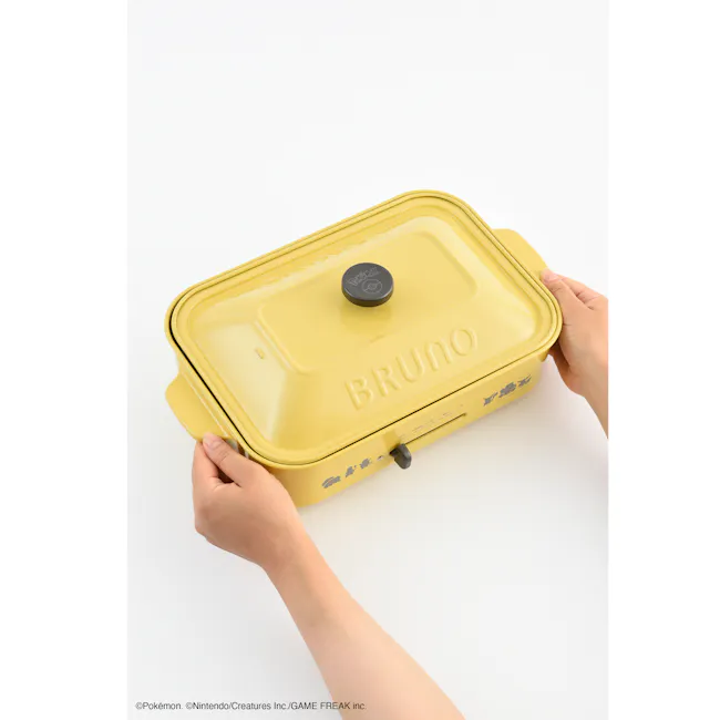 BRUNO Pokémon Compact Hot Plate - 9 - Yellow kitchen appliance, "Bruno" branding, lid with "Poke Pokémon" logo, person