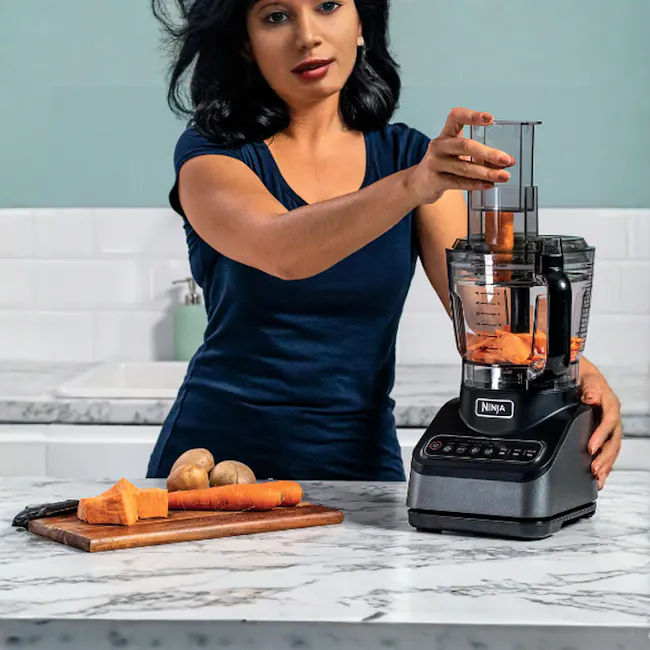 Ninja Professional Food Processor - 3 - woman using Ninja blender, carrot pieces on cutting board, kitchen countertop, black