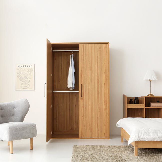 Mirans 2 Door Wardrobe - Oak - 4 - Wooden wardrobe with clothes hanging, light gray upholstered chair, minimalist decor