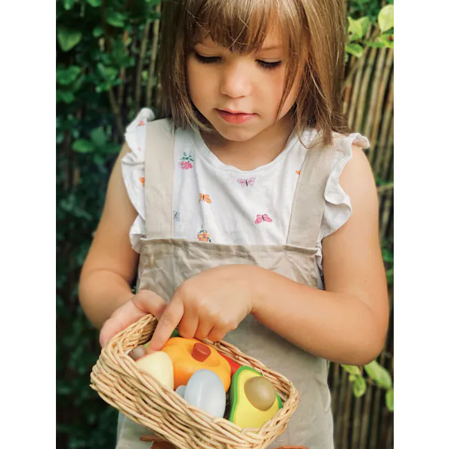 Tender Leaf Toy Kitchen - Veggie Basket - 3 - Child, young girl, outdoors, wearing dress, holding basket, colorful toys