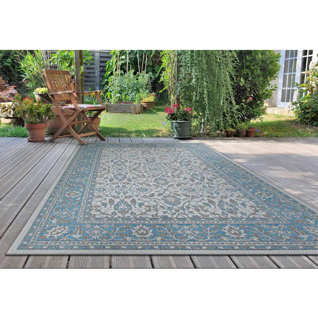 Carmoux Flatwoven Rug - Azure (3 Sizes) - 2 - Wooden deck, blue and white patterned rug, wooden chair, lush green garden