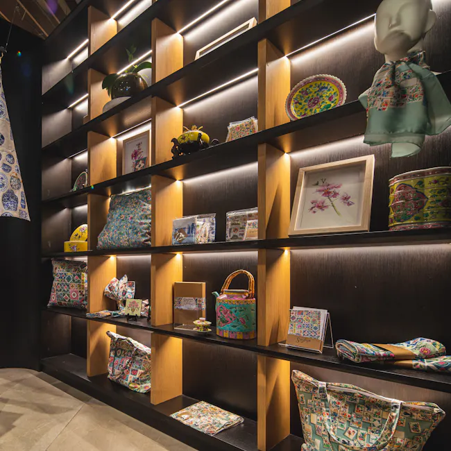 Singlapa Peranakan Teapots Tea Towel - 5 - Shelves with colorful bags, framed artwork, decorative plates, mannequin head