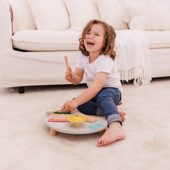 Bubble Wooden Music Table - 3 - Child playing with toys on carpet, smiling, white couch, wooden spoon, colorful blocks