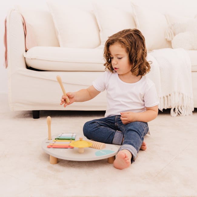 Bubble Wooden Music Table - 4 - Child playing with wooden drum, sitting on carpet, white sofa in background, white blanket