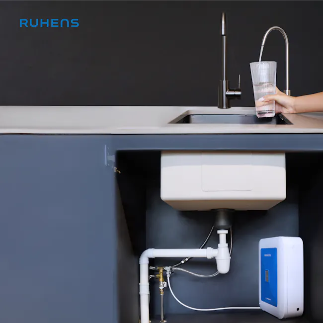 Ruhens MonoSink Water Purifier - 5 - Underneath the faucet, a hand fills a clear glass with water. Kitchen sink area with a